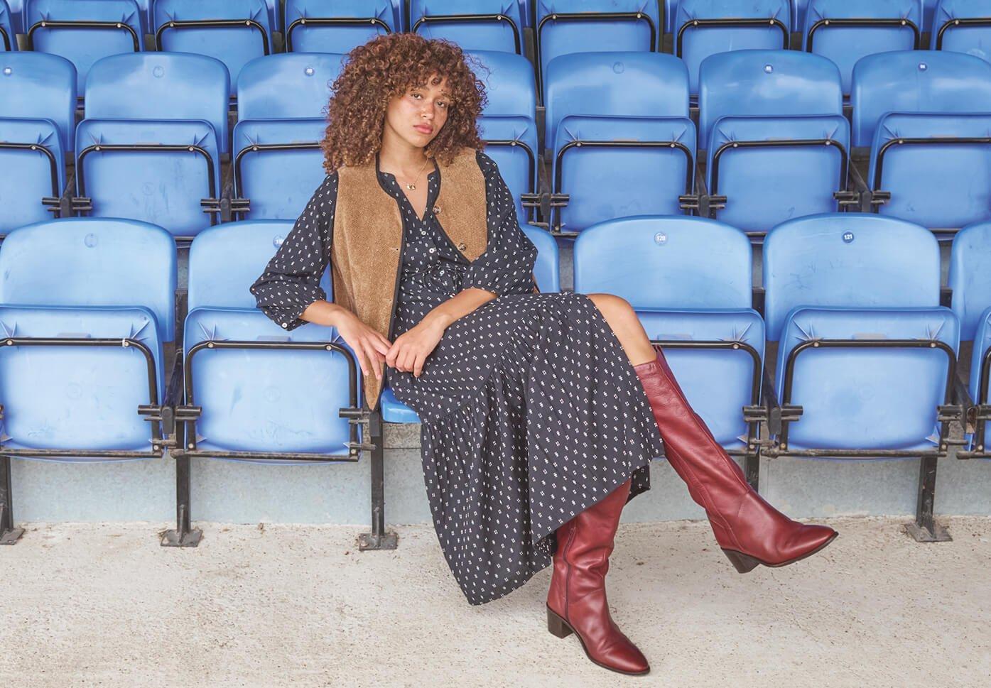 a woman sitting on a blue stadium seat with a red dress