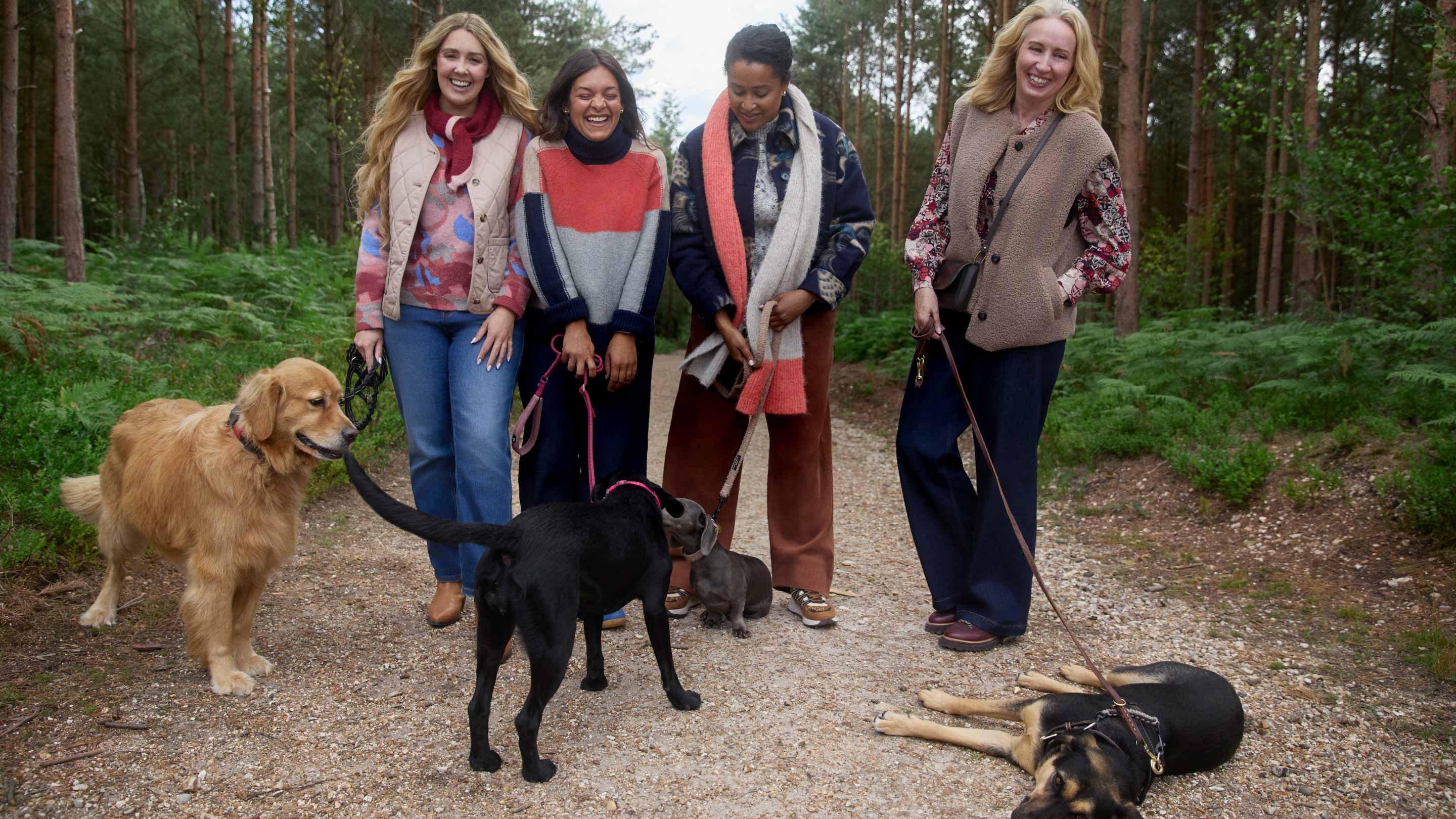 four women are standing on a dirt road with their dogs