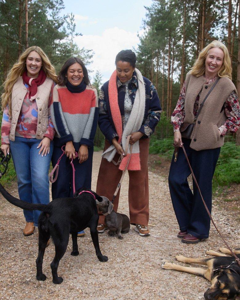 four women are standing on a dirt road with their dogs