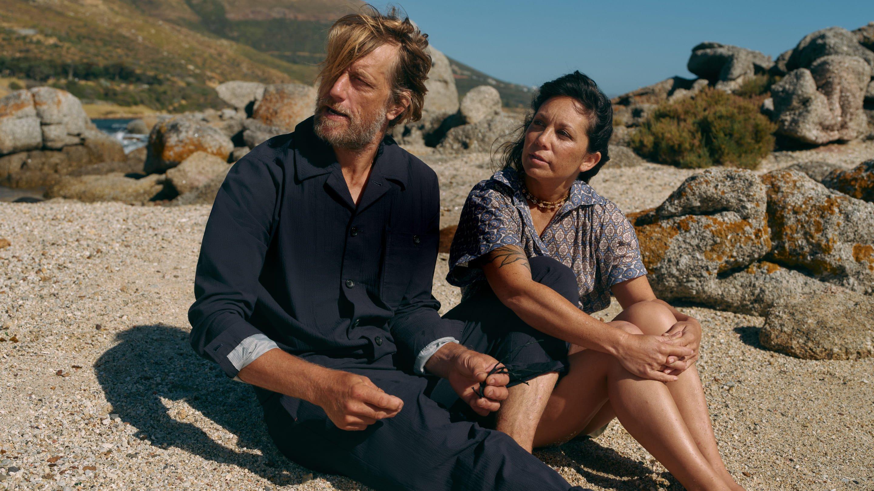 a man and woman sitting on a rock in the middle of a beach