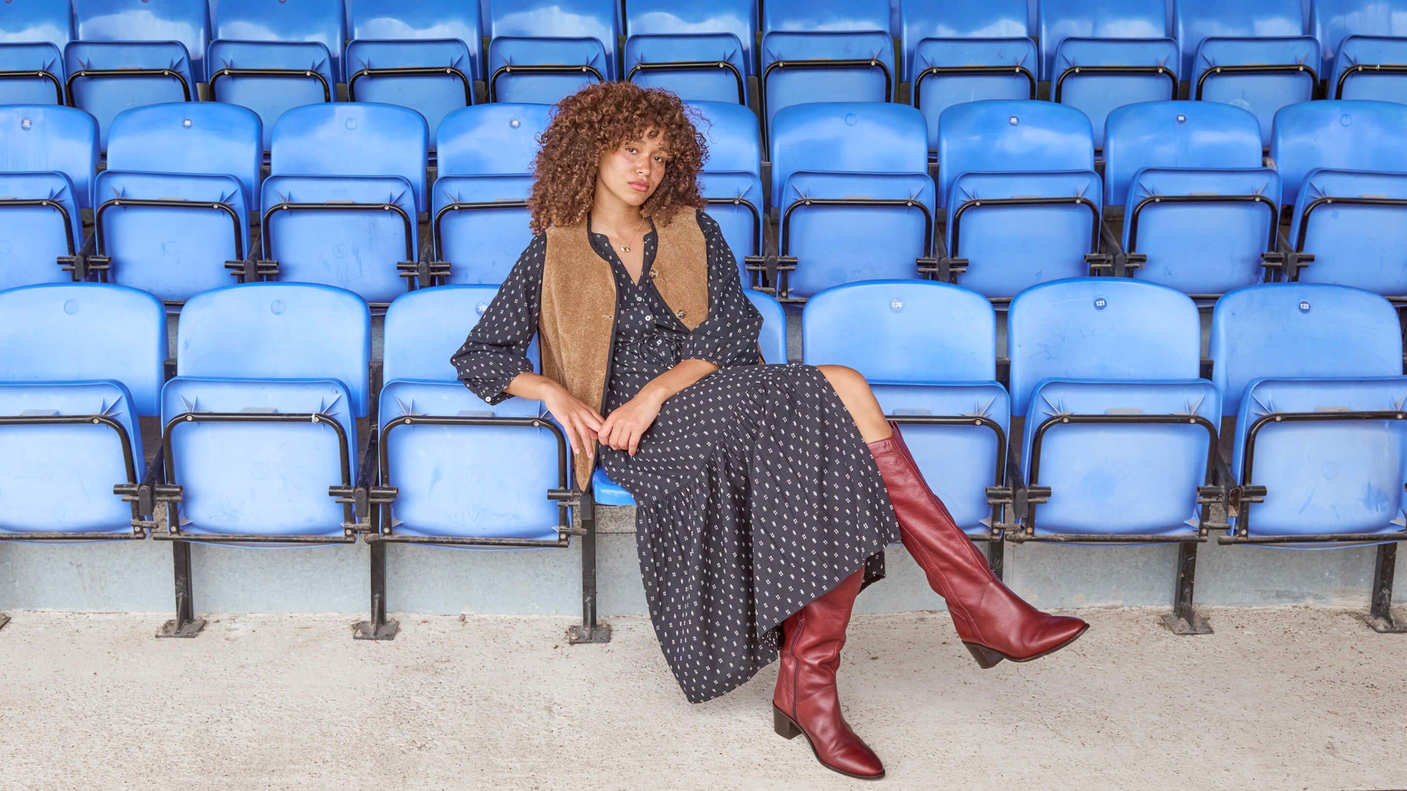 a woman sitting on a blue stadium seat with a red dress