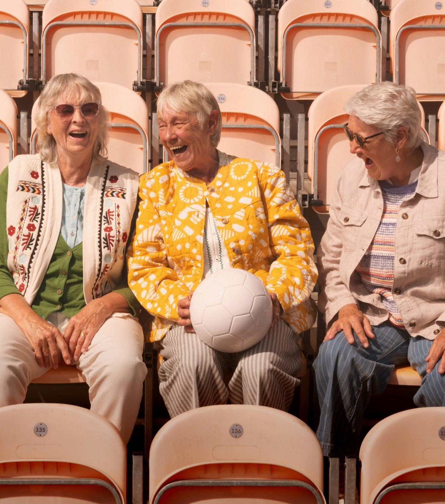 three women sitting in a row of bleachers with a ball