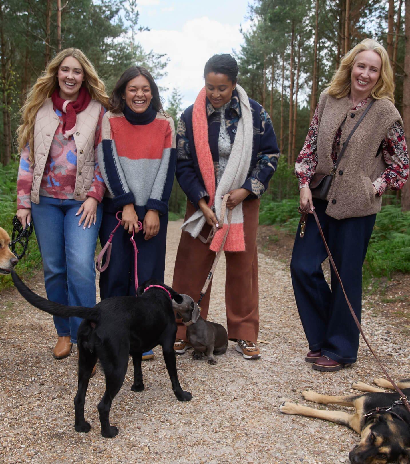 four women are standing on a dirt road with their dogs