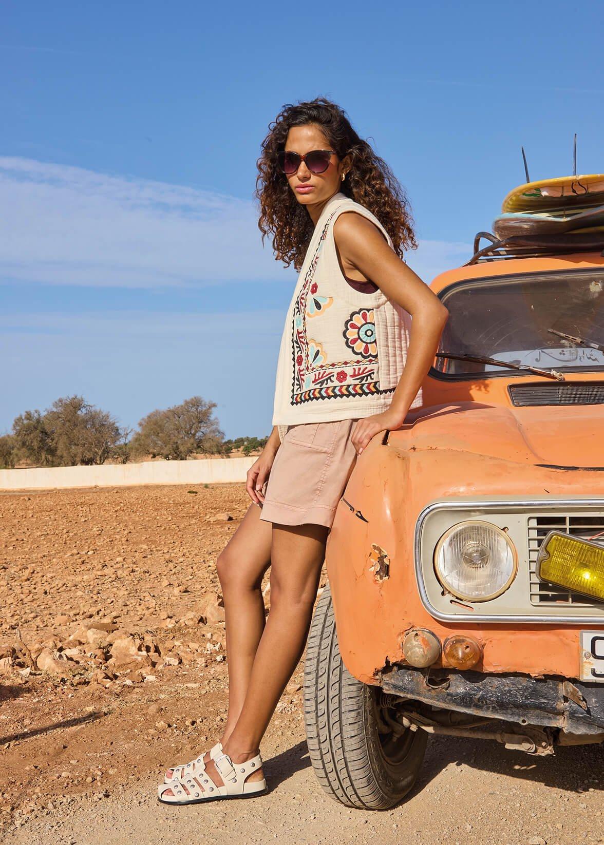 a woman wearing a gilet leaning against a car in the desert
