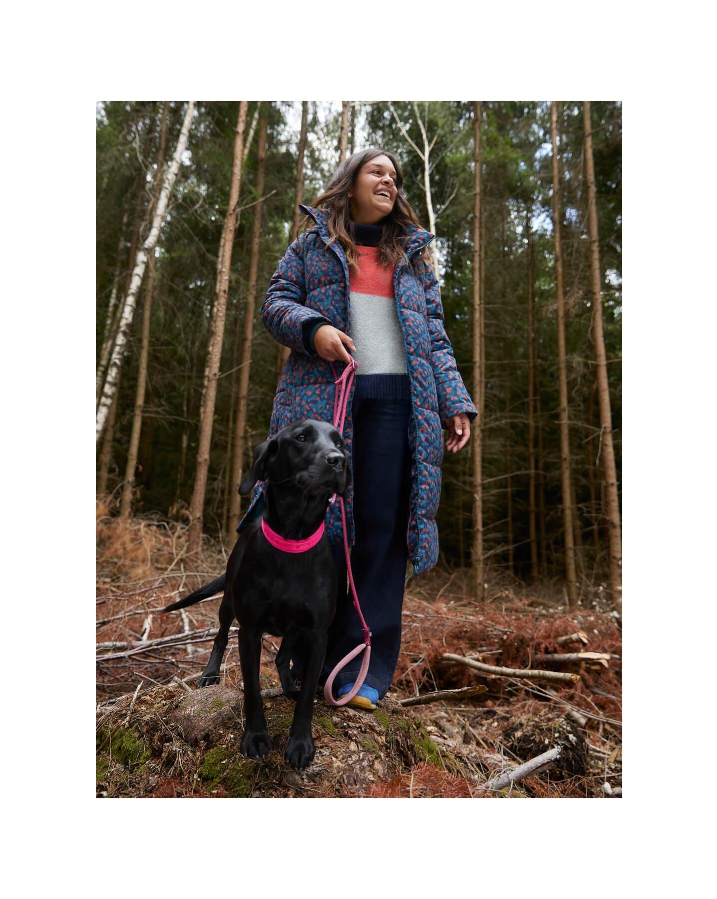 a woman in a coat and a dog on a leash in the woods
