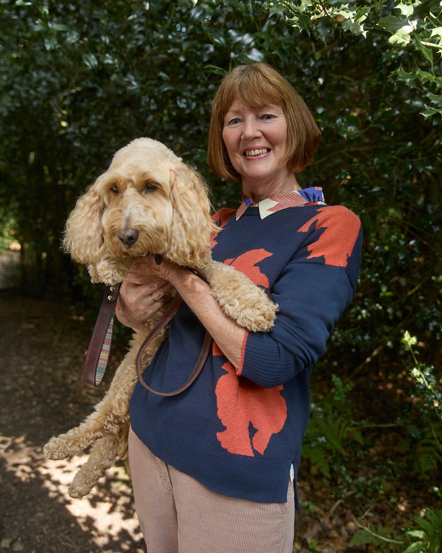 a woman holding a dog in a park with trees and bushes