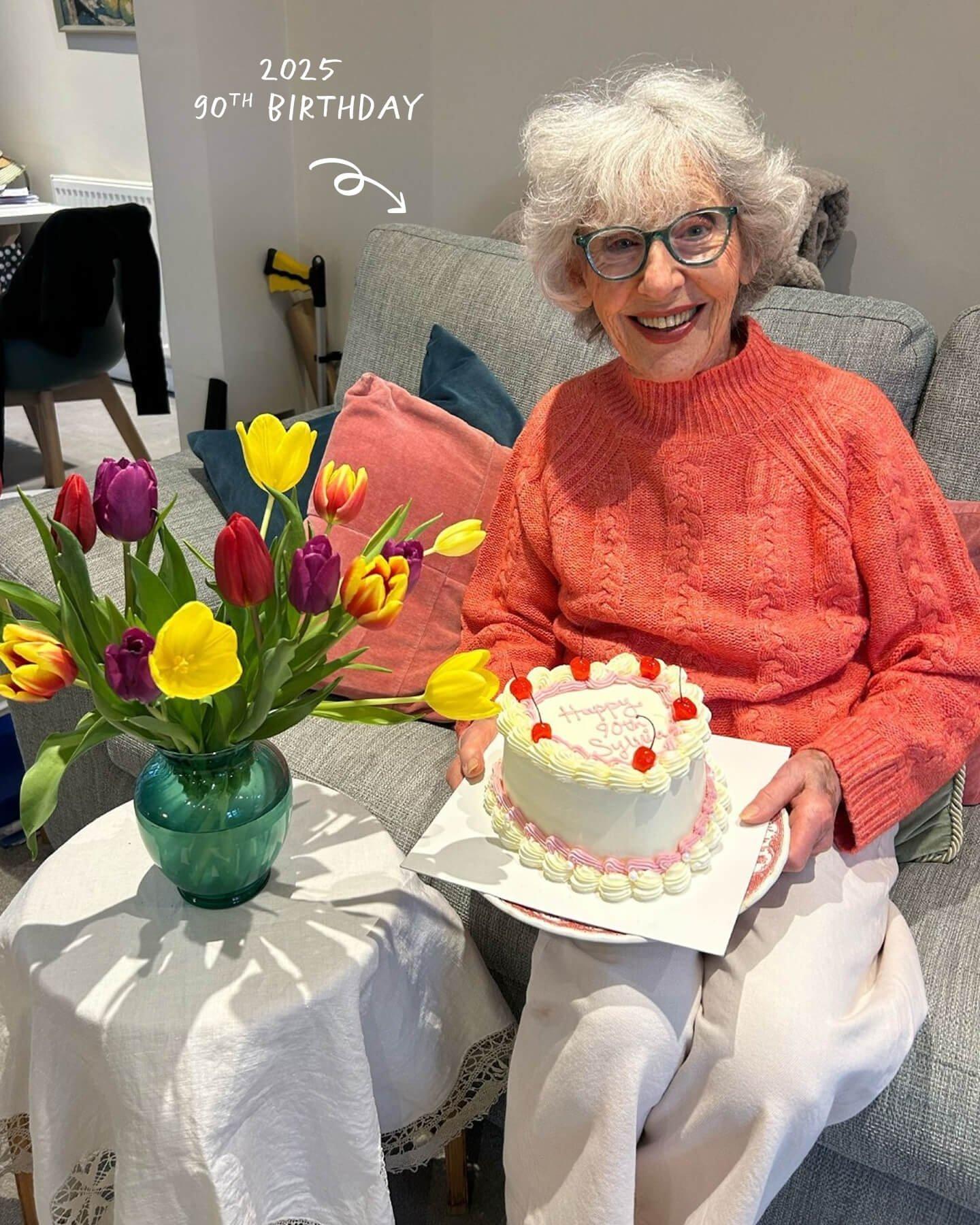 an older woman holding a cake and flowers on a couch