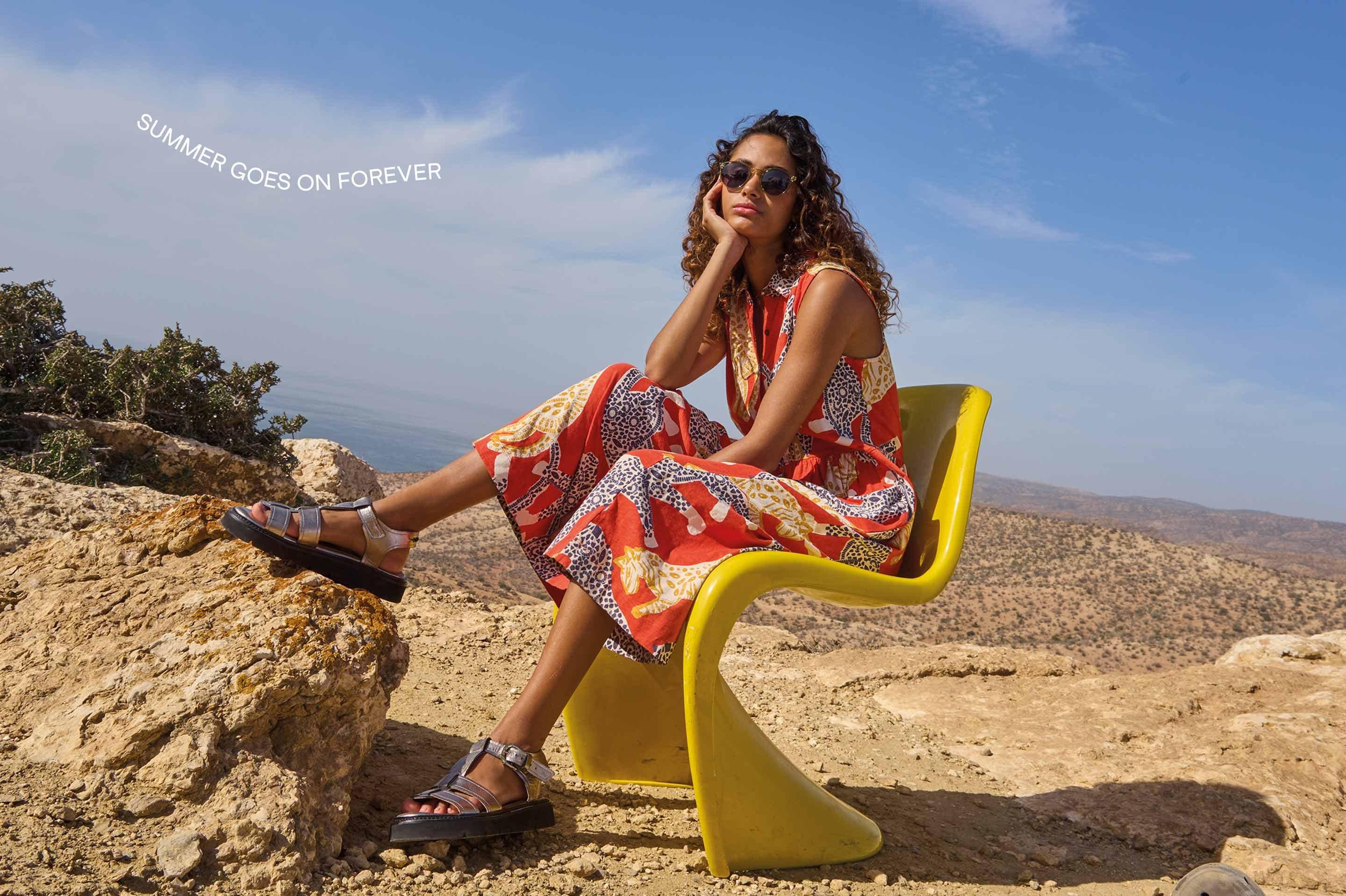 a woman sitting on a yellow chair on a rock in a maxi dress