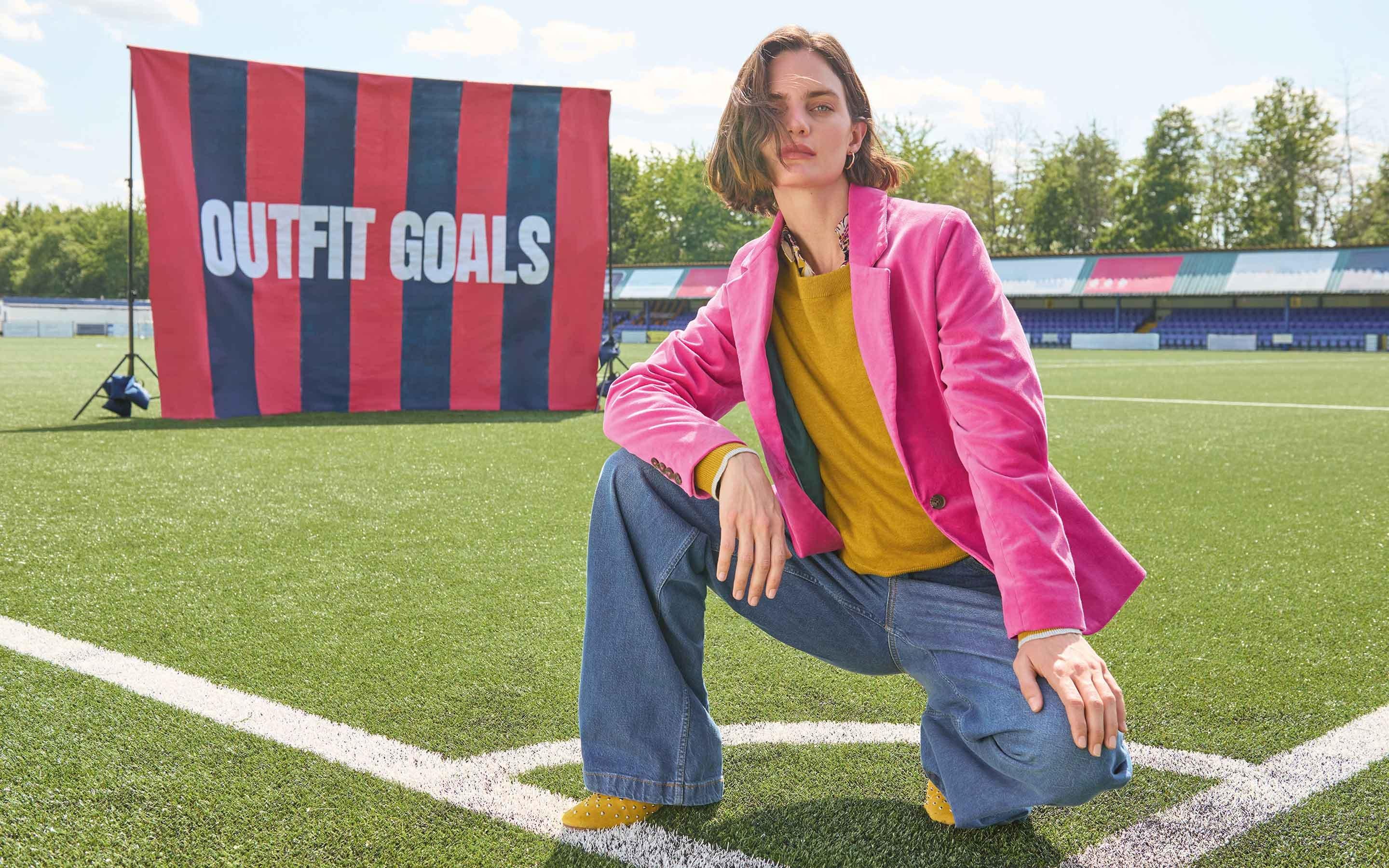 a woman in pink jacket kneeling on a football field
