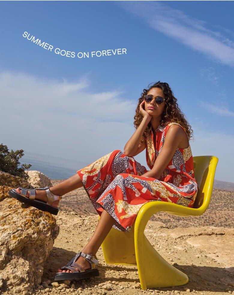 a woman sitting on a yellow chair on a rock in a maxi dress