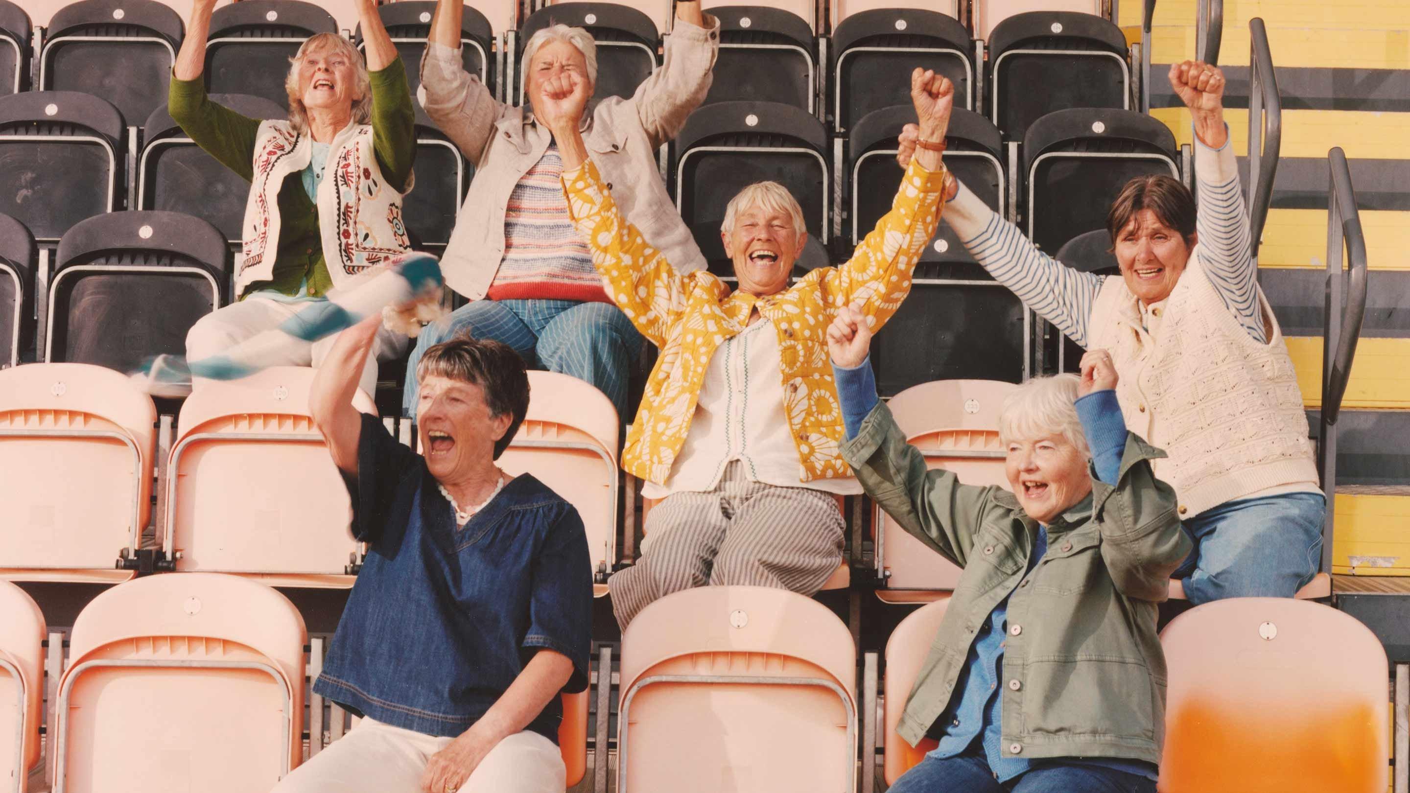 a group of women sitting in bleachers with their hands up