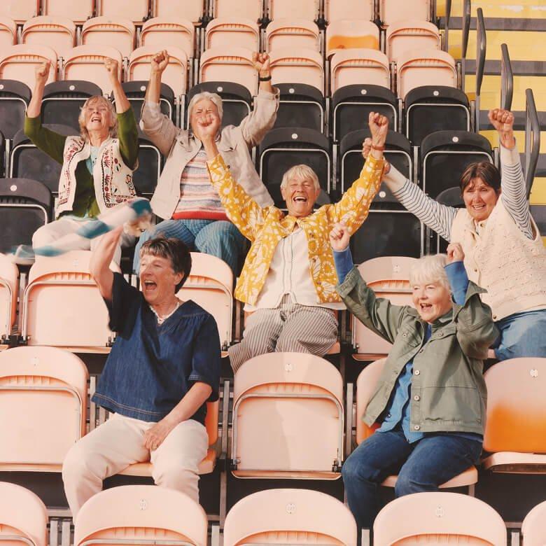 a group of women sitting in a stadium with their hands up