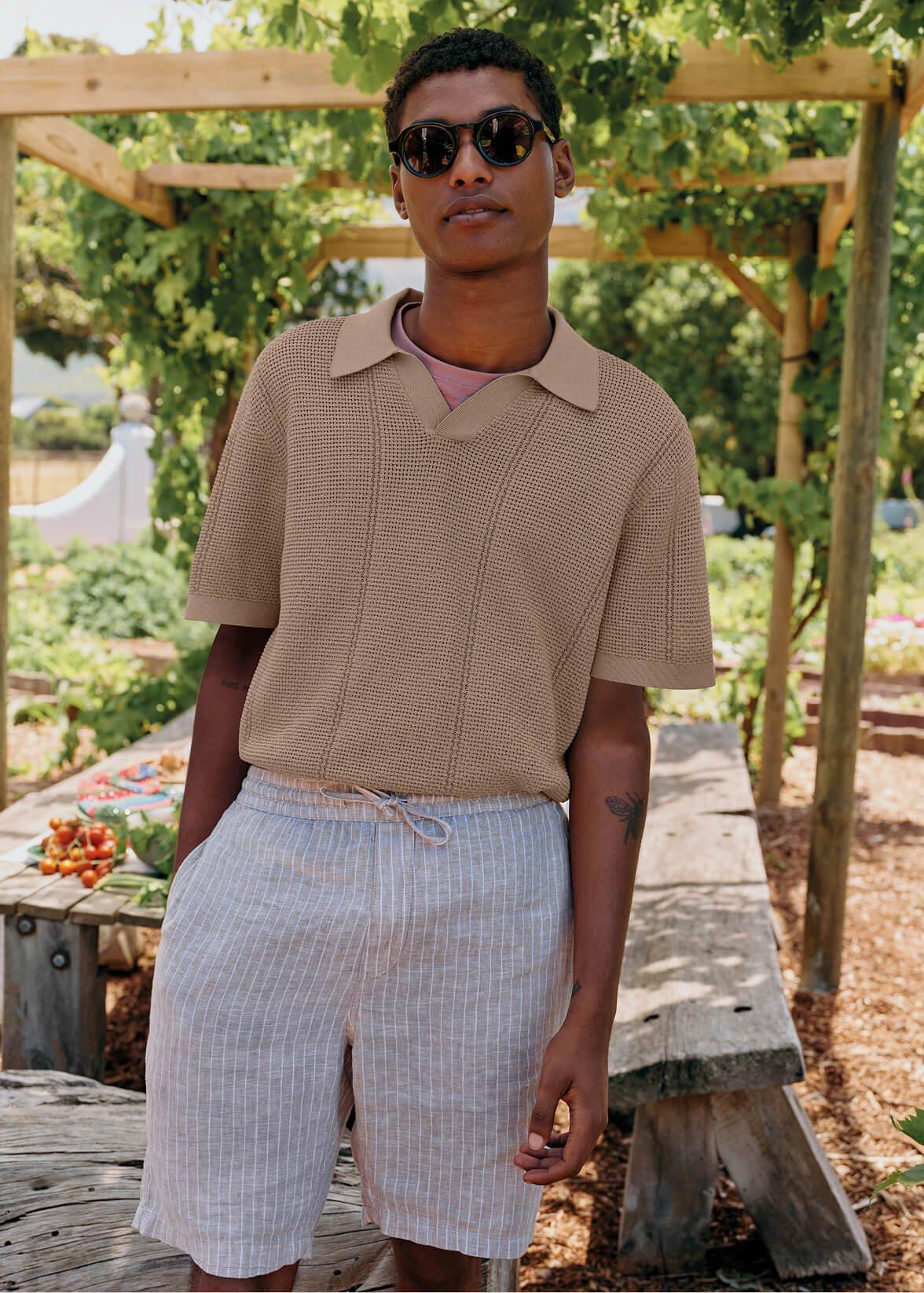 a man in a tan shirt and shorts standing in a garden