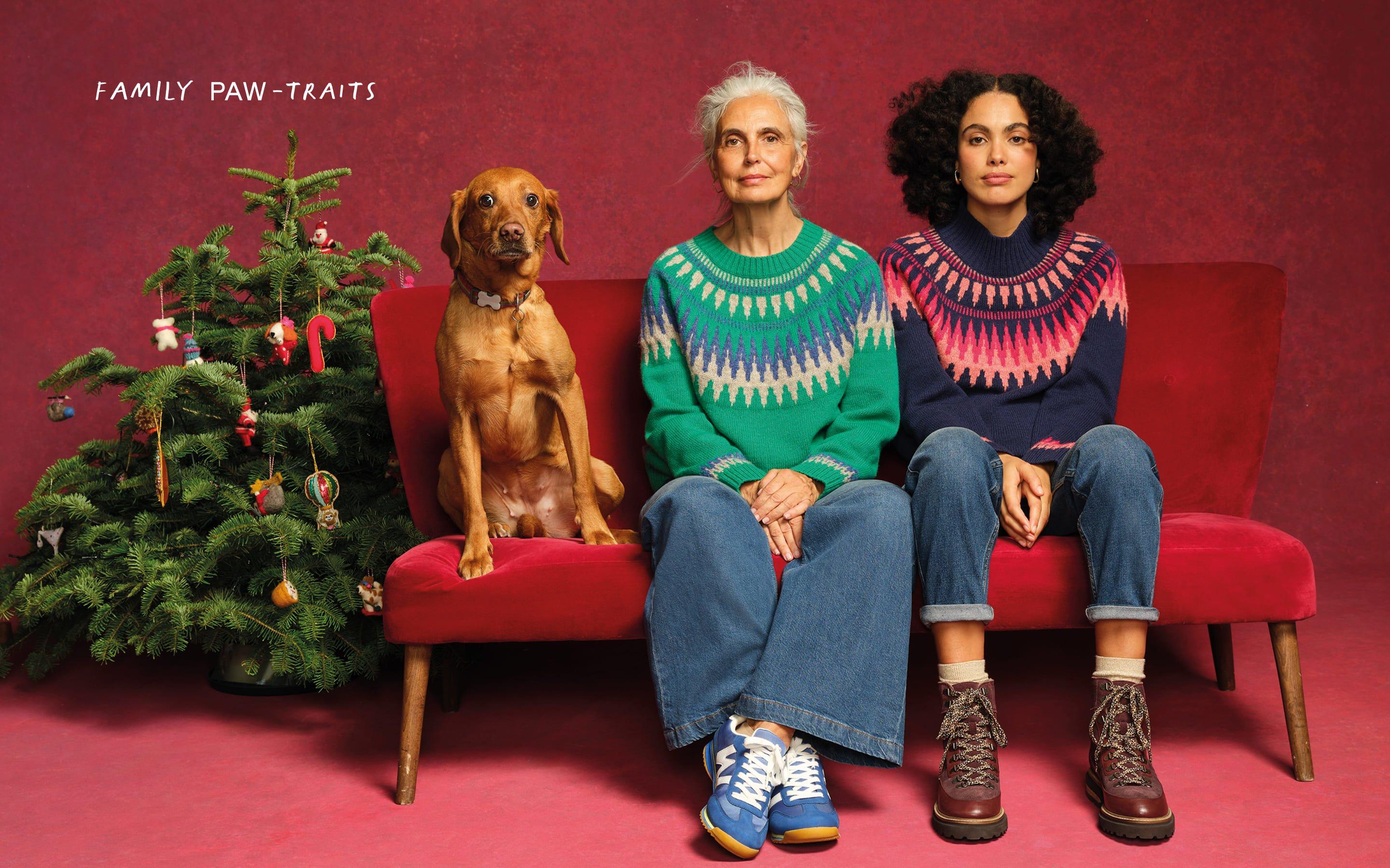 two women and a dog sitting on a red couch in front of a christmas tree