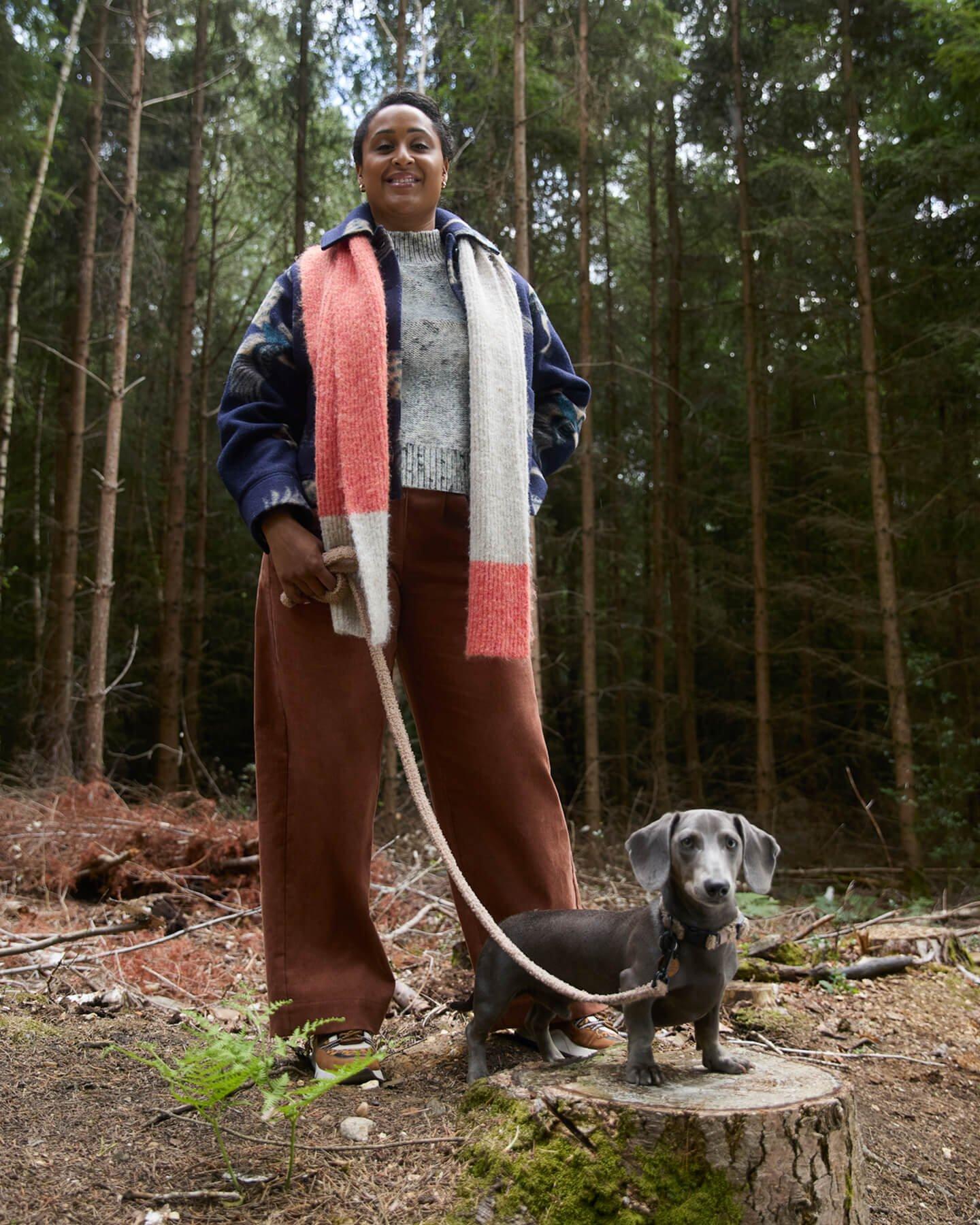 a woman standing on a stump with a dog on a leash