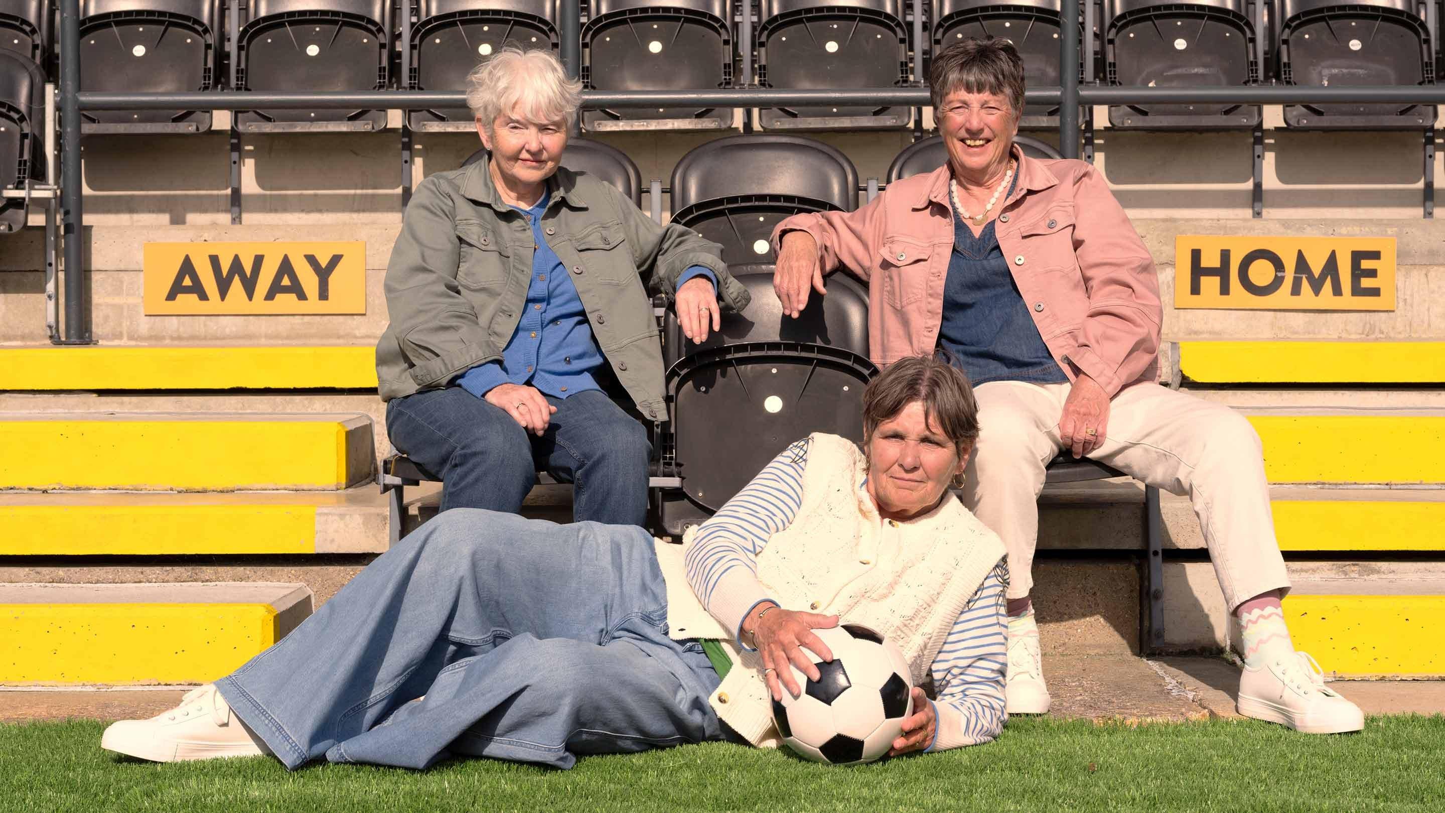 three women sitting on bleachers with a soccer ball