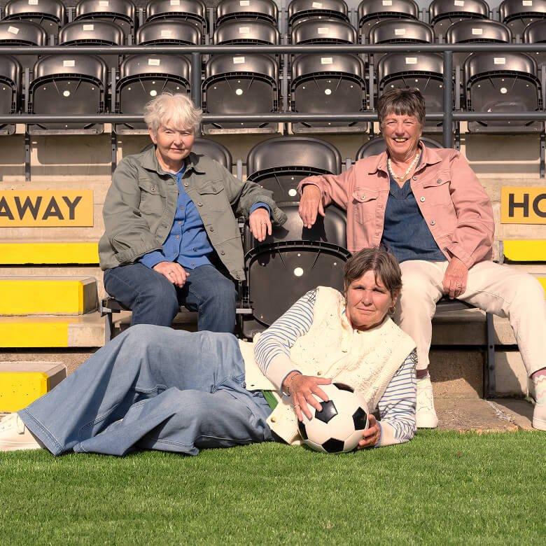 three women sitting on bleachers with a soccer ball