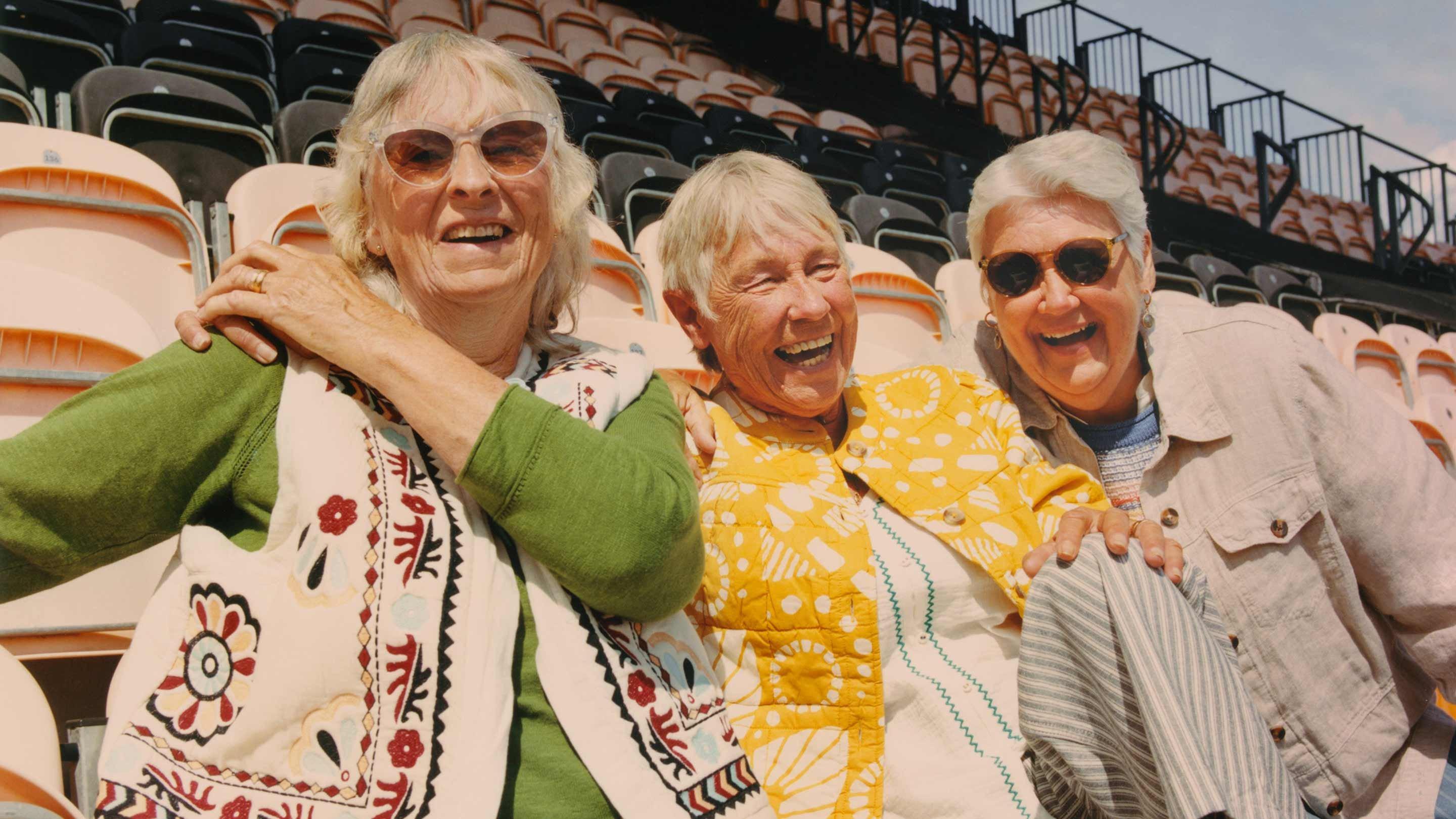 three older women sitting on bleachers wearing White Stuff clothing