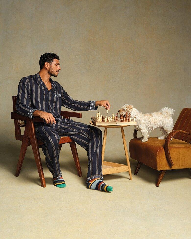 a man sitting in chair playing chess with a dog