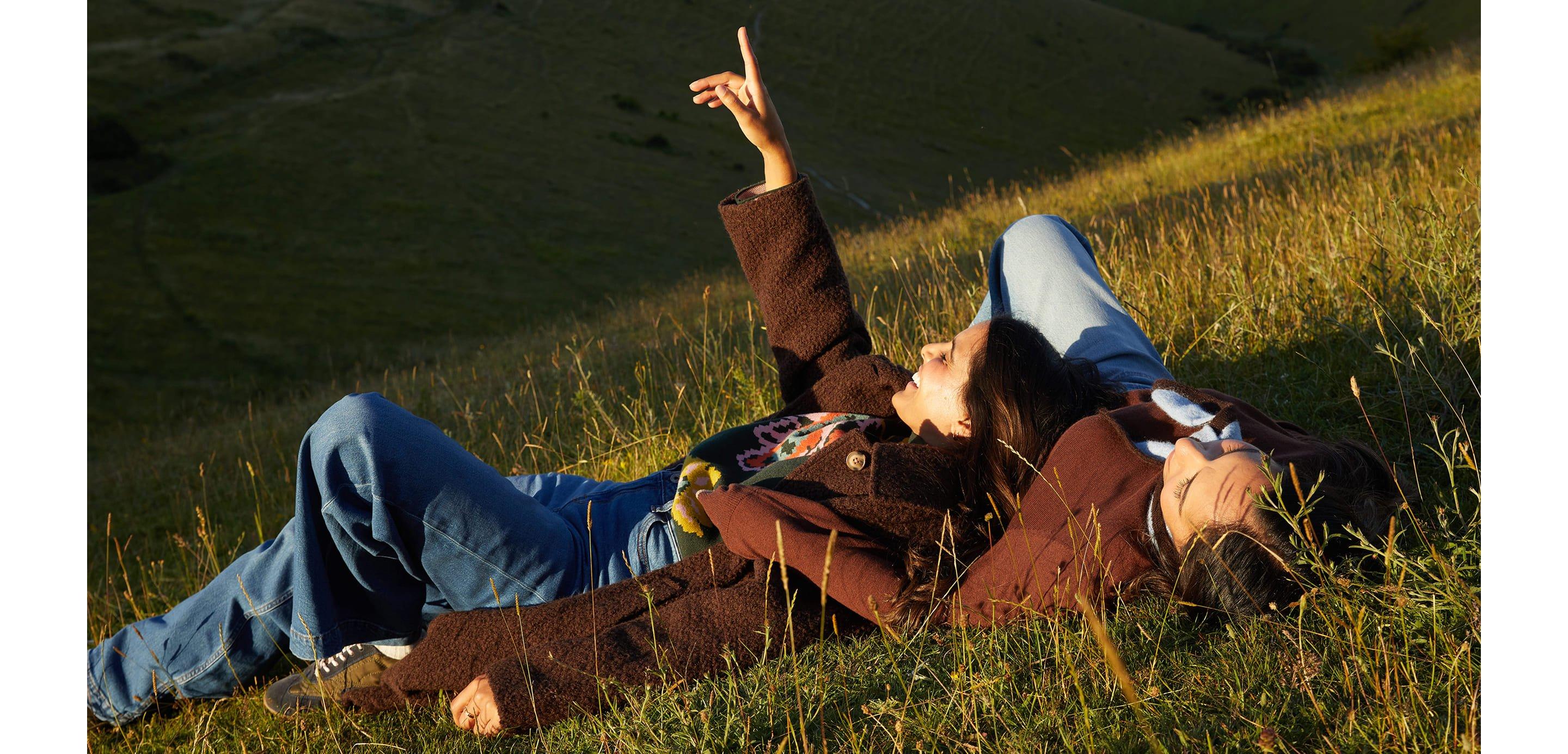 a man and woman laying in a field pointing up at the sky