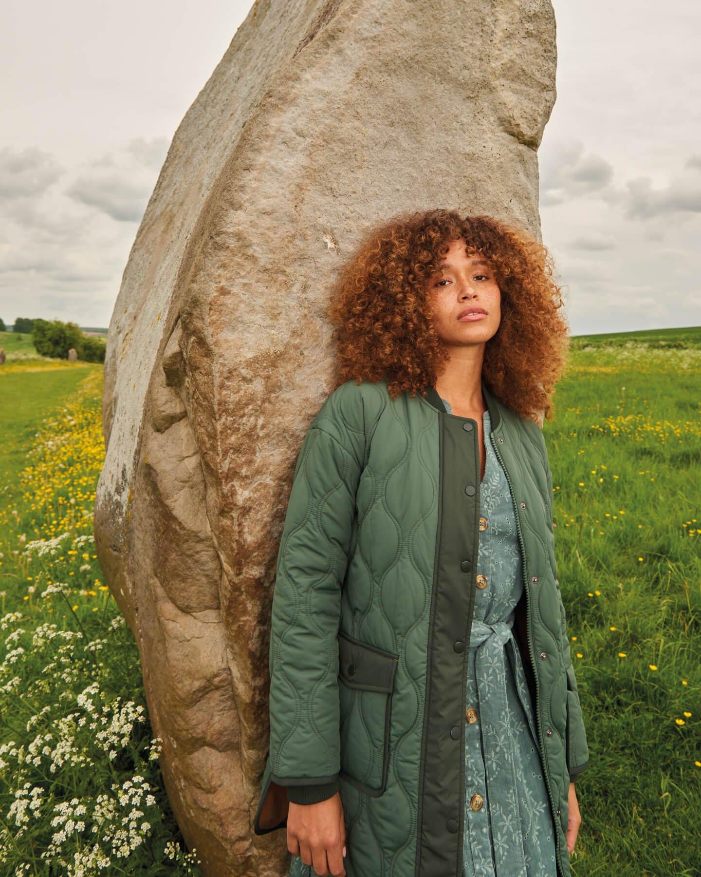 WOMAN LEANING ON STONE WEARING QUILTED JACKET