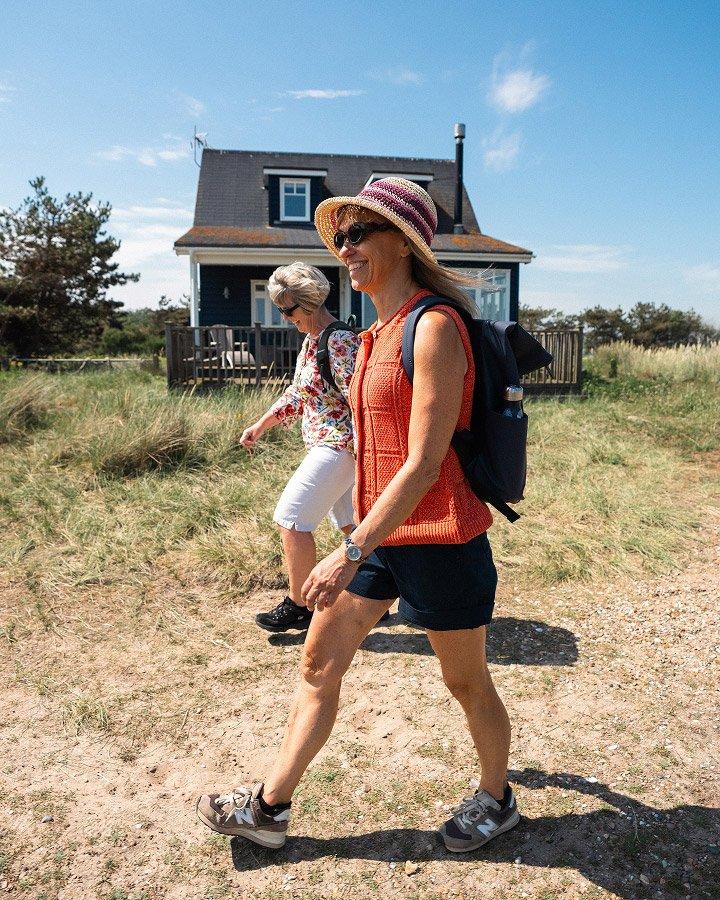 two women walking in a field with a house in the background