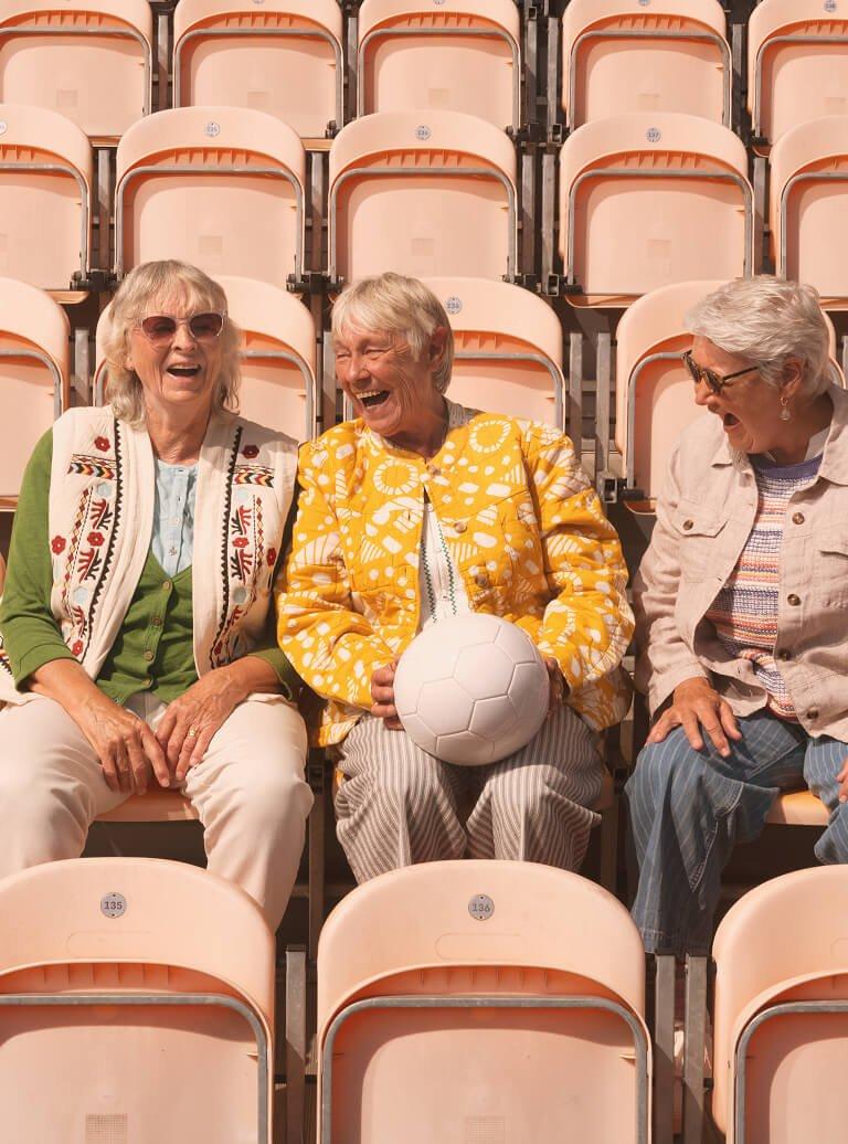 three women sitting in a row of empty seats with a ball
