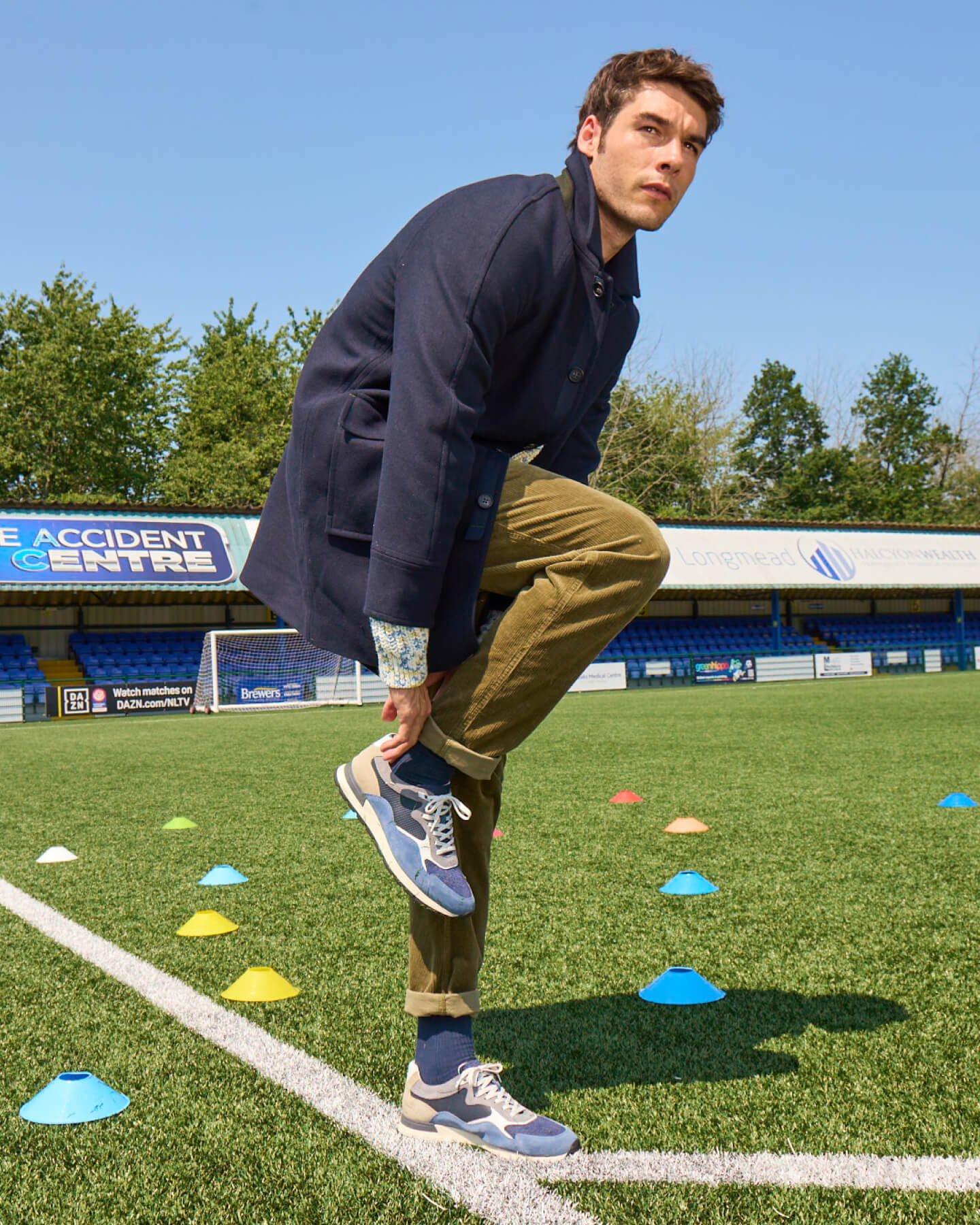 a man in a jacket standing on a football field with cones