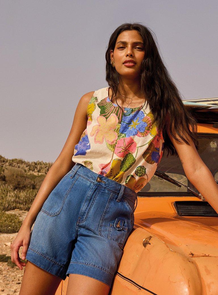 a woman leaning against a small orange car with a surfboard on top