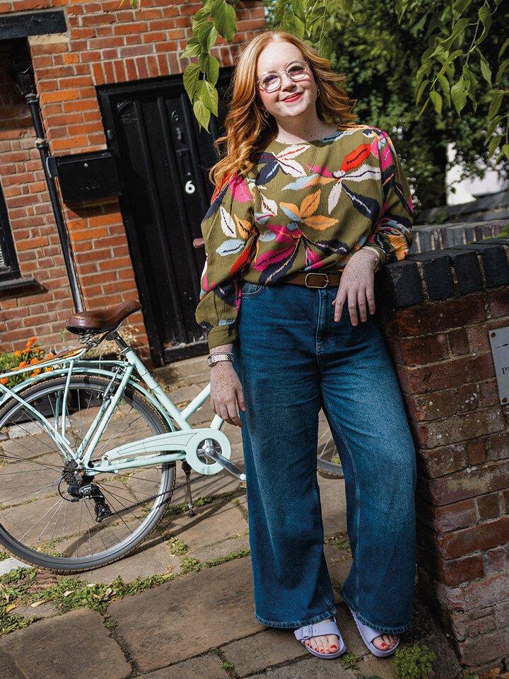 a woman leaning against a brick wall wearing a printed jersey top
