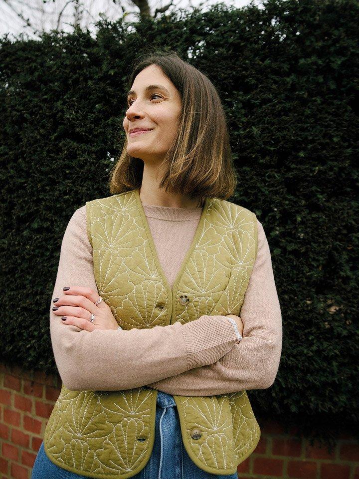 a woman standing in front of a hedge wearing a gilet
