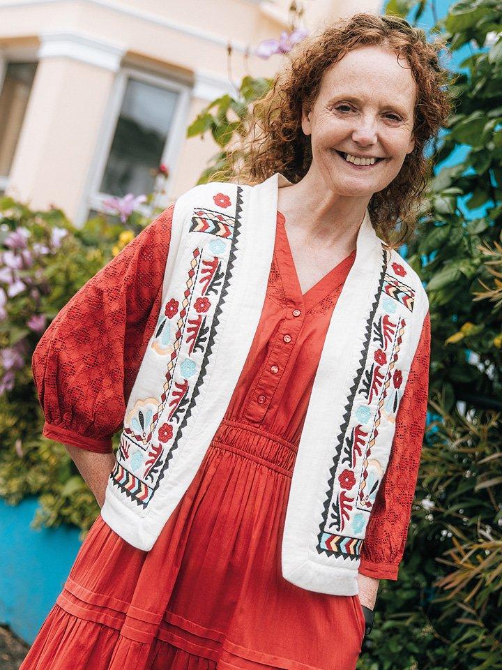 a woman in red White Stuff dress and gilet standing outside in front of a building