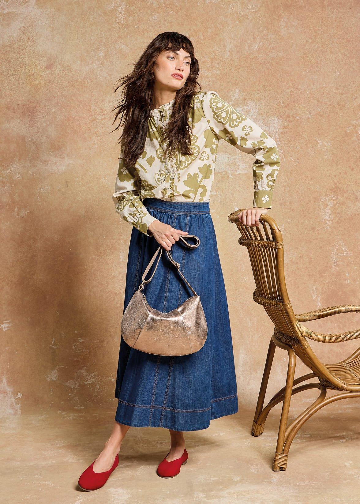 a woman in a skirt and a shirt standing next to a chair