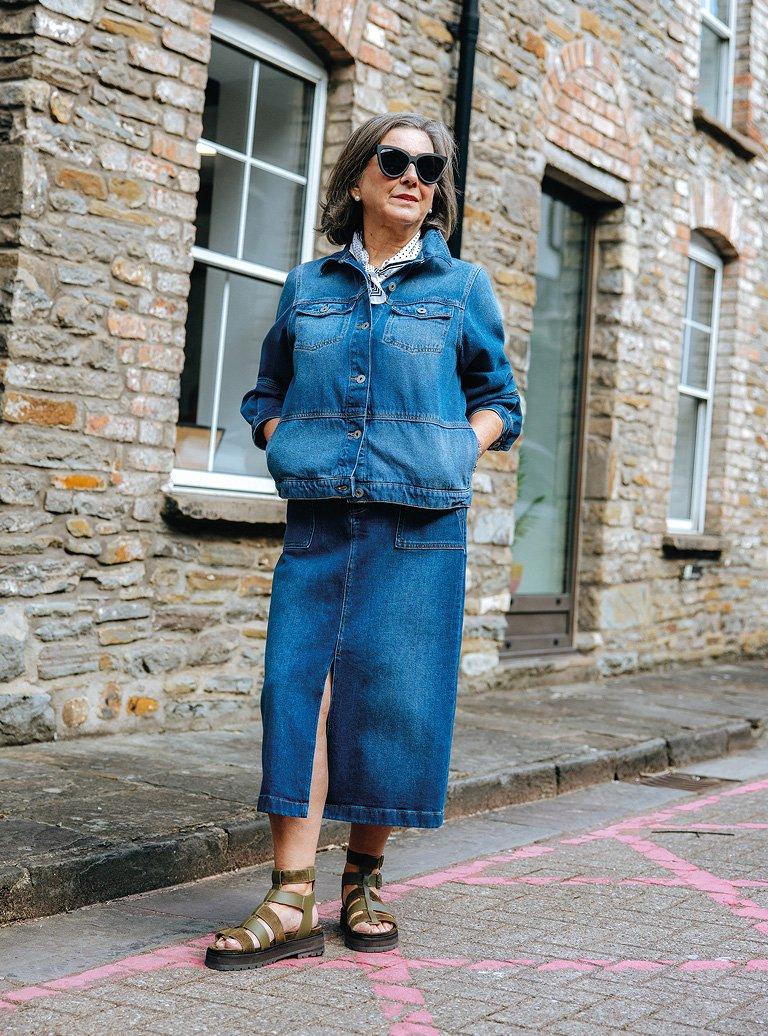 a woman in a denim skirt and sandals standing on a street corner