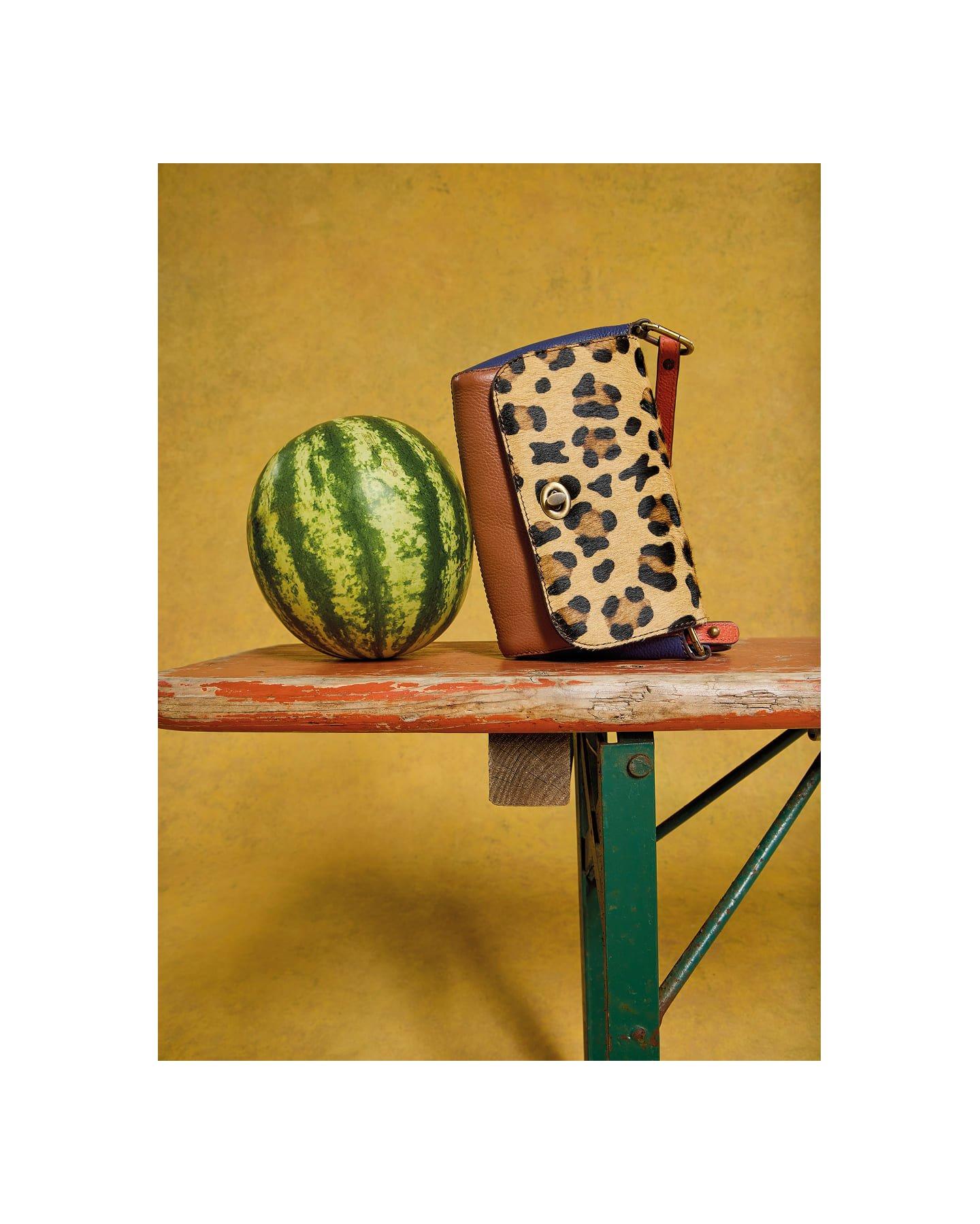 a watermelon and a handbag on a table next to a wall
