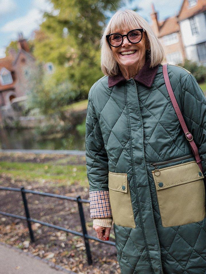 a woman in a green coat and glasses standing on a sidewalk