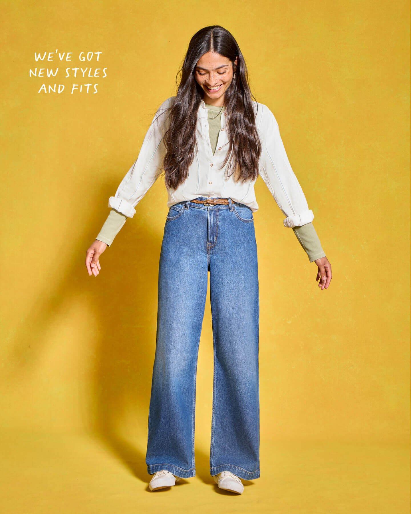 Woman in blue jeans and white shirt stood against a yellow background.