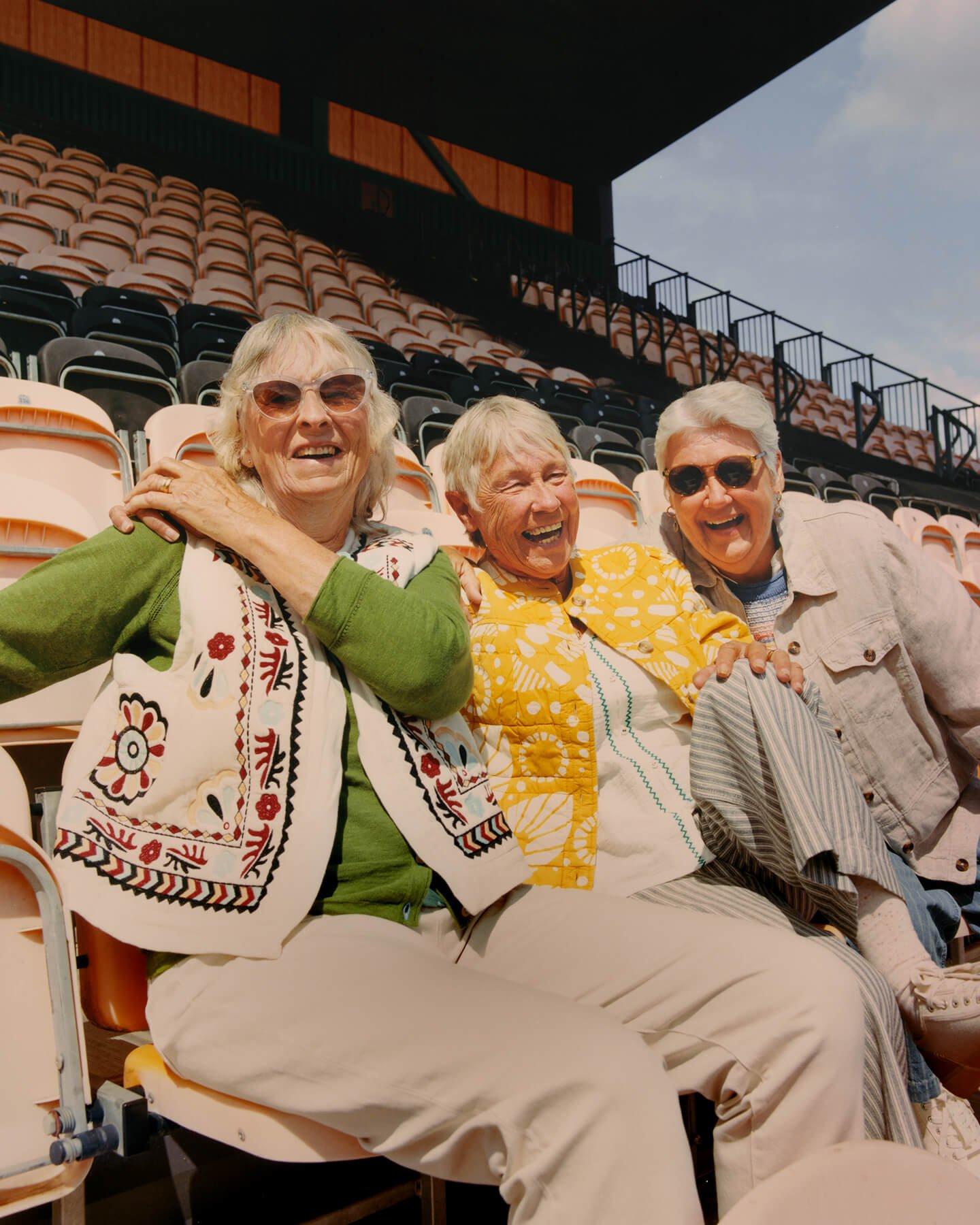 three women sitting in a stadium with their arms around each other
