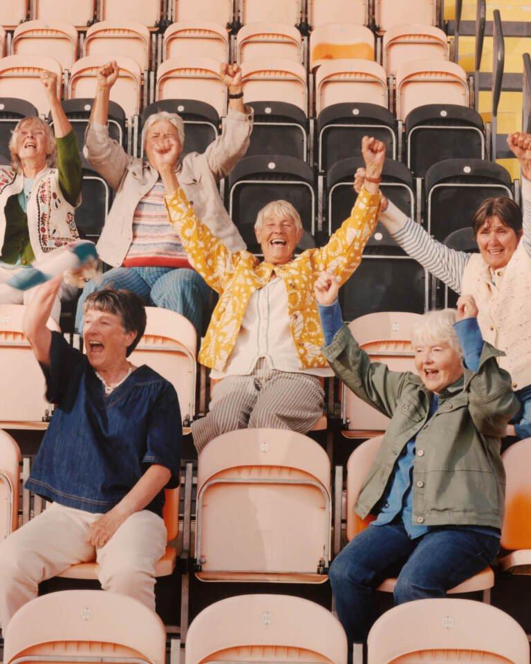 a group of people sitting in a football stadium with their hands up cheering on the lionesses