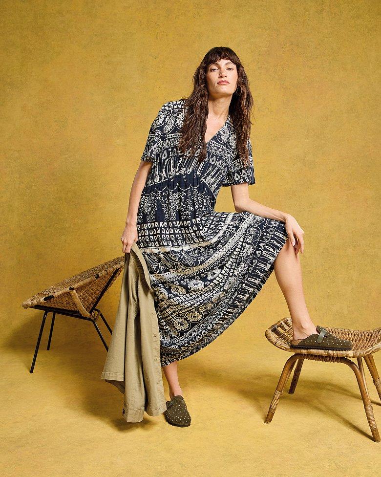 a woman in a dress holding a jacket posing on a stool