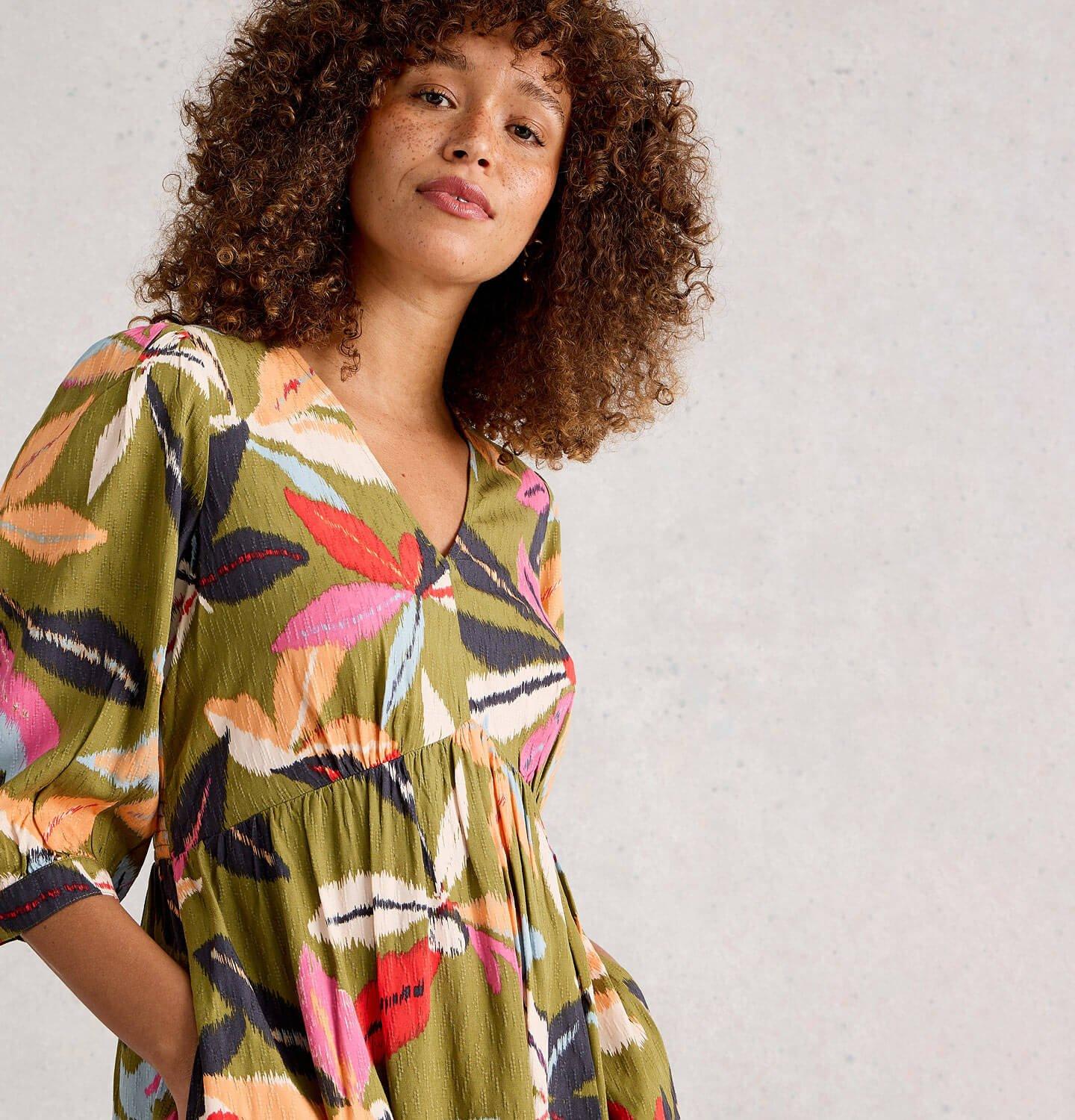 a woman posing in a green multi coloured dress with hands in pockets.