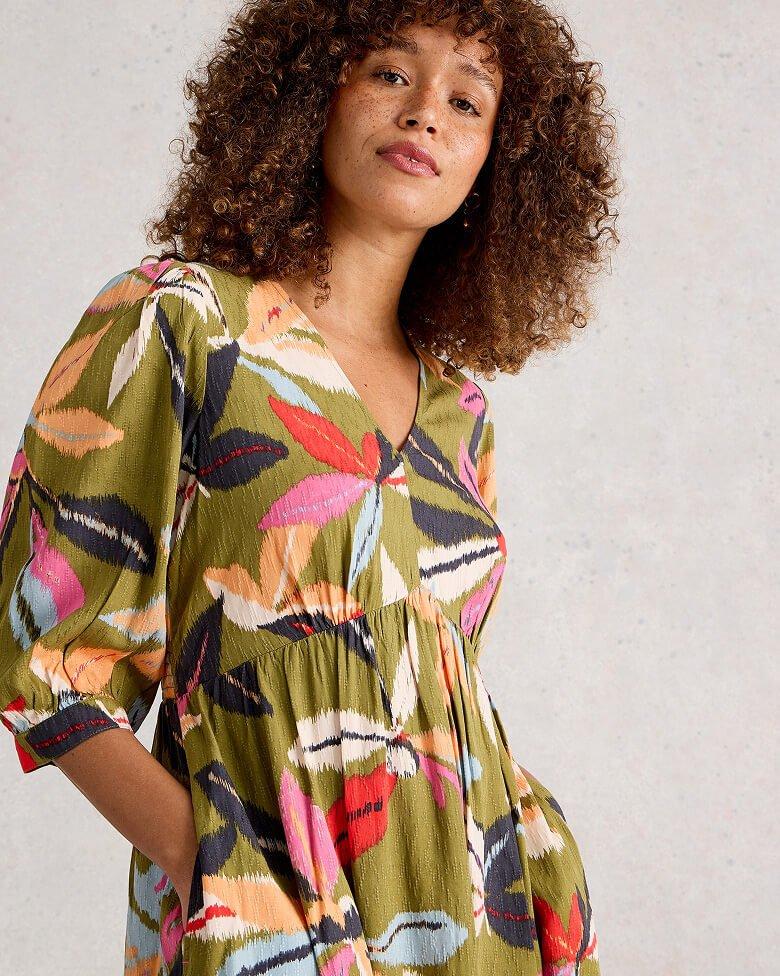 a woman posing in a green multi coloured dress with hands in pockets.