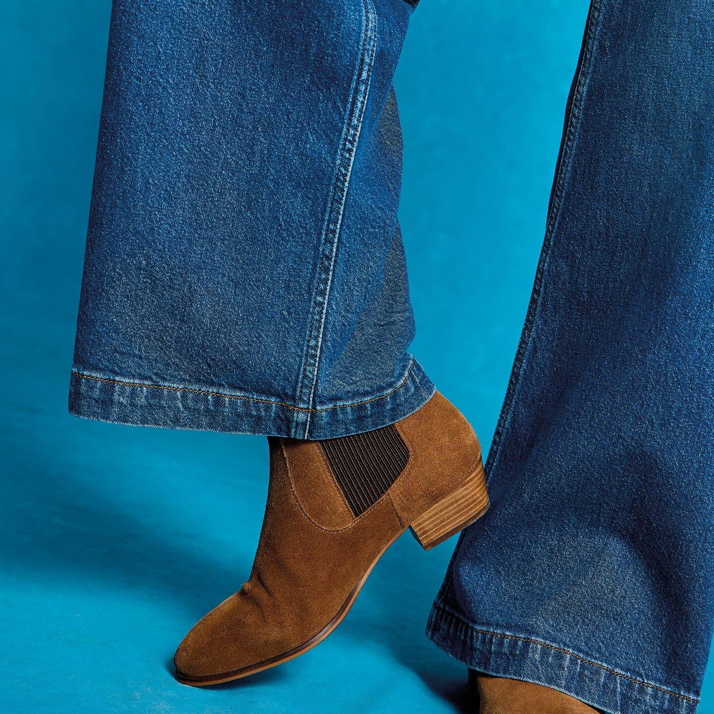 a person wearing brown boots and jeans standing on a blue background