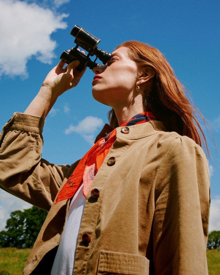 a woman looking through binoculars in a field of grass