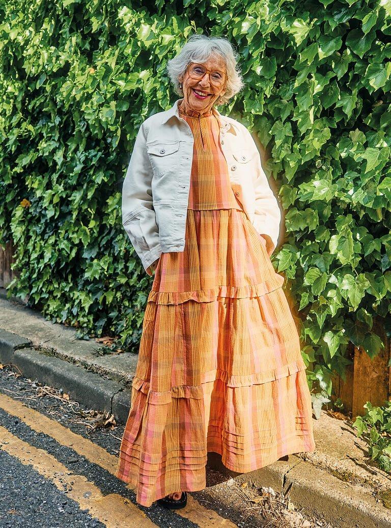 an older woman in a long dress standing on the side of the road