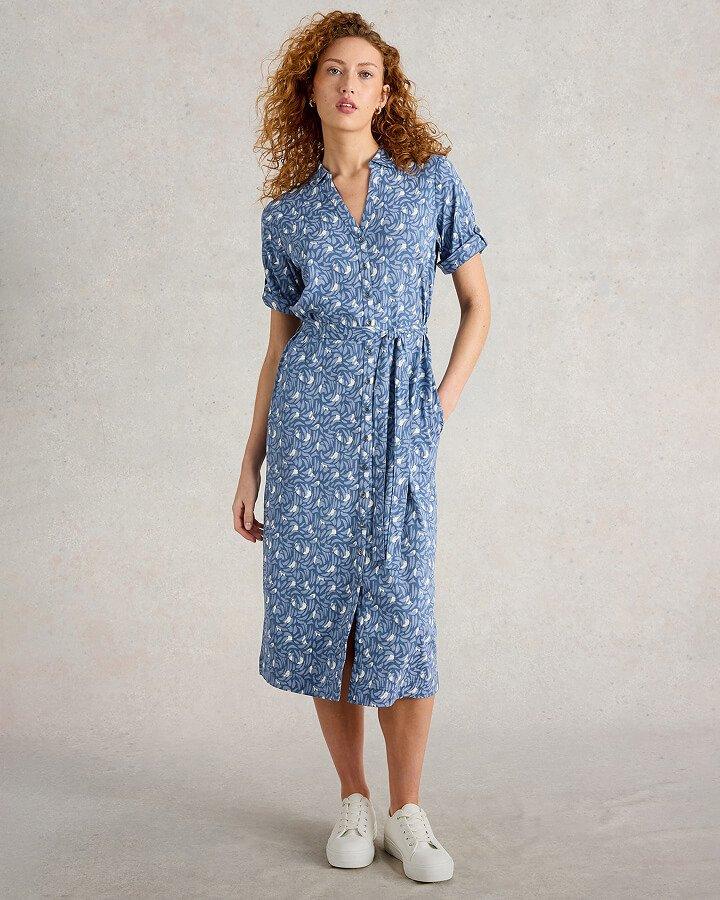 a women standing with her hand in pocket wearing a blue printed short sleeve midi dress and white canvas trainers