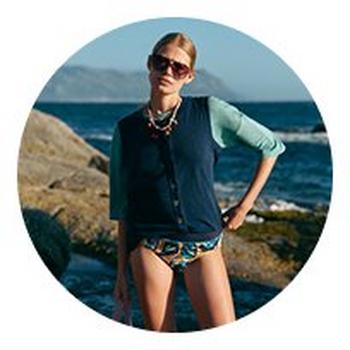 a woman in a bathing suit standing on a rock by the ocean