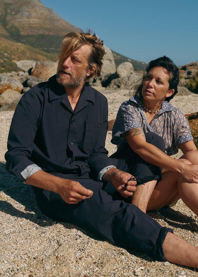 a woman walking along the beach with a hat and a bag