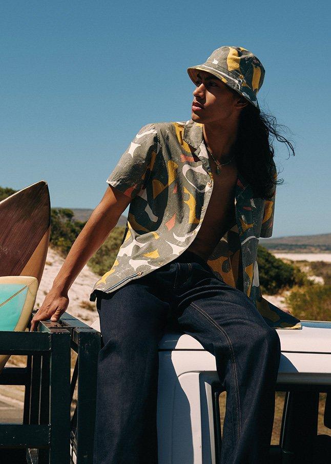 a man in a hat leaning on the back of a truck with surfboards