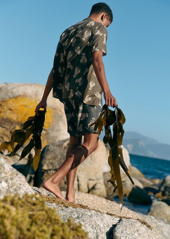 a man walking on a rocky beach carrying a bunch of seaweed